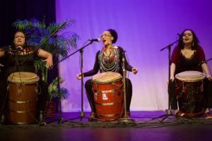 three women singing and playing large drums